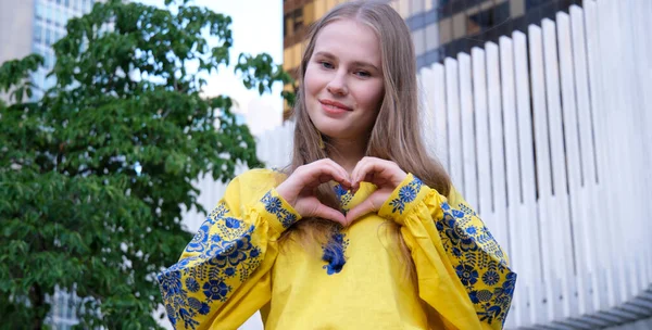 穿着黄色毛衣的年轻姑娘微笑着 用双手表现出她的心 爱的标志 黄色的Vyshyvanka 乌克兰传统服饰 在大城市里年轻女子对国家和平的热爱 — 图库照片