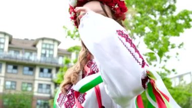 Geleneksel halk imajıyla saçını düzelten sevimli genç kız Ukraynalı kadın. Rüzgâr esiyor ve buklelerini geliştiriyor. Bir sürü çiçekli güzel çelenk. Doğanın doğal güzellikleri.