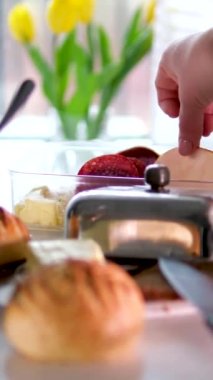 Kadın eli, yemek masasından bir parça jambon alır. Şeker kasesi, arka planda süt çörekleri, beyaz masa. 