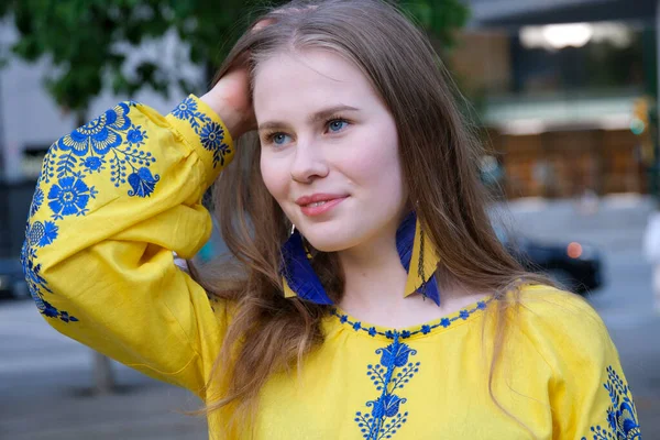 用双手拉直头发 长长的耳环挂在蓝色和黄色绣花蓝色花中 女孩穿着绣花衬衫 乌克兰民族服装 一件黄色衬衫 — 图库照片