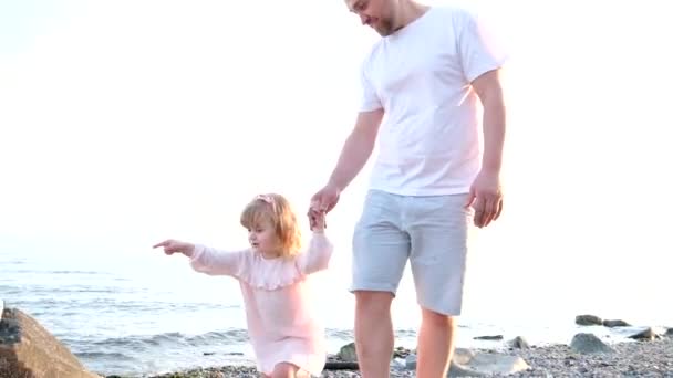 喜ばしい父親は娘と一緒に歩く 3歳の女の子の周りに見える彼女の指喜びビーチで家族の休暇兄弟足は見える家族の喜び愛 — ストック動画