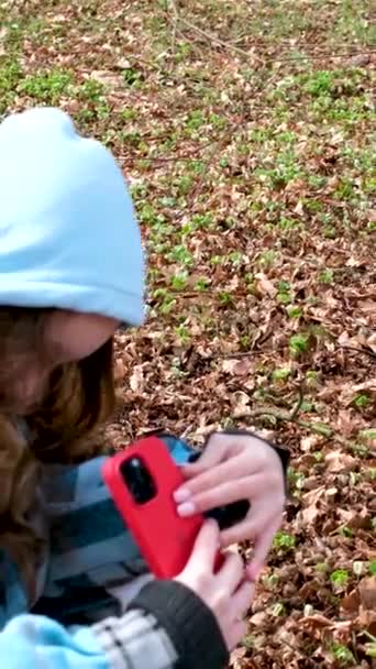 秋天或春天的秋天 一个拿着红色手机的女孩在公园里从最底层拍到了一个红色盒子里的照片 这个盒子里是一个戴着头巾的蓝色夹克的女孩的手机 — 图库视频影像