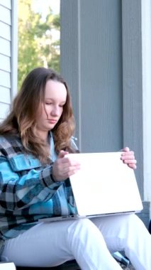  Kız okulunu bitirmiş verandada oturmuş dizüstü bilgisayarı kapatmış yan yatmış ödevini yaptıktan sonra dinleniyor. 