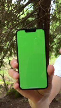 Yakışıklı İspanyol bir adam, üzerinde yeşil ekran kromatonunun durduğu bir telefon gösterir. Ormanda beyaz bir gömlek giyer. Yüksek kalite 4k görüntü