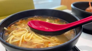 Domuz eti ve karidesli erişte çorbası Asya mutfağı sıcak vermicelli çorbası ve siyah kase. Kırmızı oryantal kaşıkla buharlı yemek sağlıklı öğle yemeği Koreliler, Tayvan Vietnamlılar doğru dürüst yemek yer.