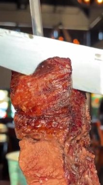 Et lokantası büyük bir bıçakla büyük bir parça et kesti. Arka plandaki restoranda tanınmayan insanlar görülüyor. Cafe bira, et, domuz eti, dana eti ve orta pişmiş et.
