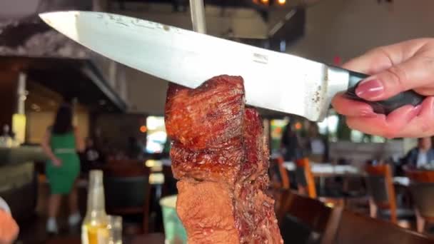 肉料理店はテーブルの上に巨大なナイフでバーベキュー肉の大片を切り取ります 背景にあるレストランでは誰も知らない人たちがカフェに座っていますビール肉豚肉ベールジューシーな中火ロースト — ストック動画