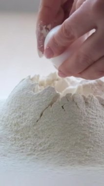 Kadın eli yakın plan beyaz tavuk yumurtasını kırar yumurta sarısı proteini un yığınına dökülür küçük damlalar el ele tutuşarak yumurta sarısı yumurtasına yavaşça ulaşır 