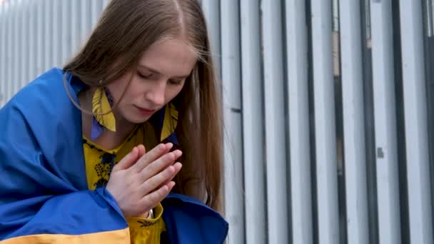 乌克兰女孩肩膀上挂着乌克兰国旗 双手交叉在胸前金发前祈祷 青春的痛苦在内心的战争中乌克兰赢得了对上帝的期望祷告请求 — 图库视频影像