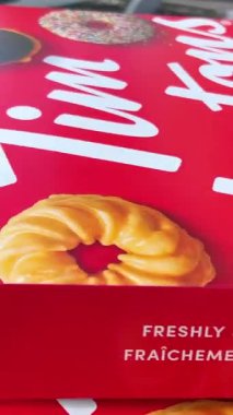 Kontrastlı ışıkta Tim Hortons çöreklerinden oluşan geniş, açık bir kutu. Bir kadın hediye olarak iki kutu lezzetli tatlı taşır, bir ikram, Canada Vancouver 07.07.2023