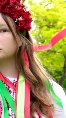 Güzel Ukraynalı genç kız büyük kırmızı çelenk içinde parlak pembe kırmızı çiçekler etrafında dönen düz saçlar saçlarında kurdele ören 
