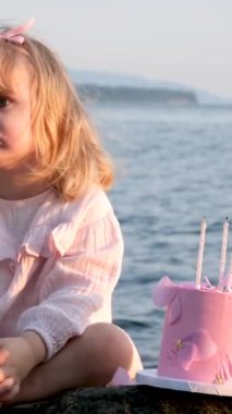 Küçük tatlı bir kız, üzgün bir şekilde oturmuş bir gölün kıyısında pastayla bacağını kaşıyordu. Yalnız kutlayan üçüncü yıl dönümü fotoğraf seansı yorgun pembe papyon elbise sarı saç