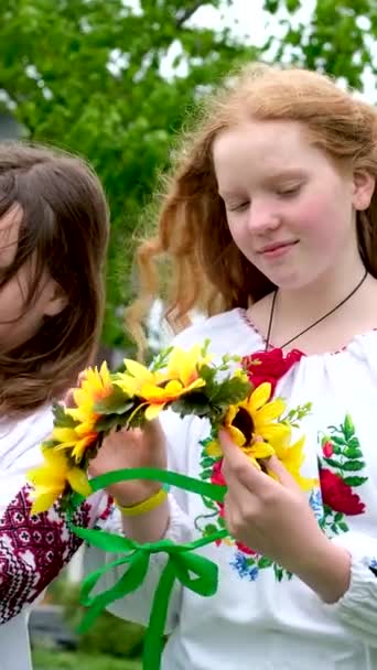 美しい若い女性が花輪を織っている庭で公園でおしゃべりを笑って歩いているひまわりの花や森の刺繍国のウクライナのシャツの花輪 — ストック動画