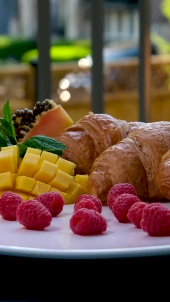 一盘浆果和烤牛角面包放在白桌上 优质覆盆子草莓芒果木瓜白盘阳台 — 图库视频影像