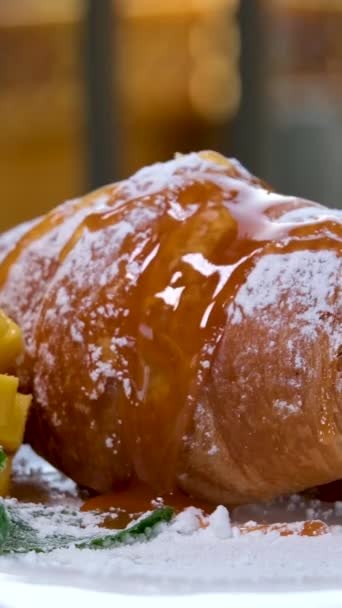 キャラメルとマンゴーのクロワッサンの上にペーストリーがのったおいしいトッピングは 朝のフレンチブレックファーストの隣に粉砂糖ミントシートを振りかけた — ストック動画