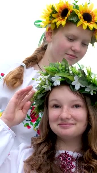 美しい若い女性が花輪を織っている庭で公園でおしゃべりを笑って歩いているひまわりの花や森の白の刺繍国のウクライナのシャツの花輪 — ストック動画