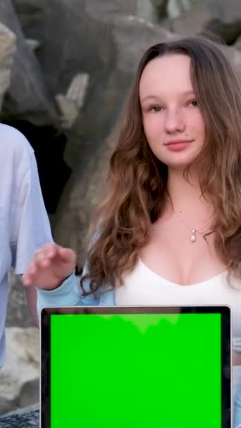 男孩和女孩坐在石头上 手里拿着笔记本电脑 绿色屏幕在为轻装做广告 青少年有趣的电影社交网络学习旅行和文字铬钥匙的位置 — 图库视频影像