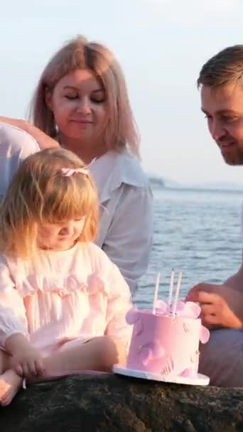 自然の中で3年の誕生日を祝うケーキの上におじぎ家族のお母さんのお父さんの息子と娘は石の上に座っています ろうそくと家族のケーキとチャット女の子は家族の子供や両親に愛を果たしています — ストック動画