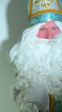 Turkuaz bir elbisesi, uzun beyaz sakalı ve Sinterklaas 'ın Noel Baba' sı Aziz Nicholas 'ın portresini taşıyan bir şapkası var.