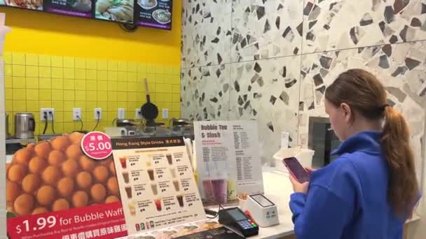 快餐快餐店泡茶 温哥华的一个穿着蓝色毛衣 拿着手机订了杯饮料的女孩 — 图库视频影像