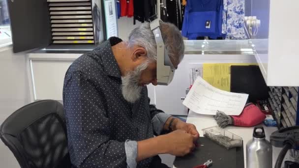 特別な虫眼鏡で時計を修理する白い髭時計職人を持つ高齢のアラブ人男性は 女性がショップの時計工房カナダバンクーバー07 2023で完成した修復メカニズムを与えます — ストック動画