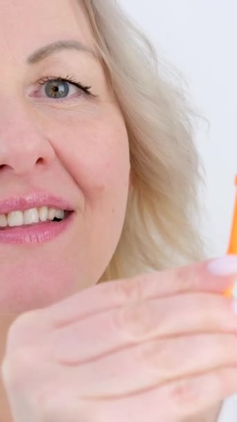 垂直ビデオだ 女性は新しいオレンジ歯ブラシを実証彼女は歯をきれいにするための特別なデバイスのキャップを削除し 適切に食品をきれいに歯を磨く方法を示しています — ストック動画