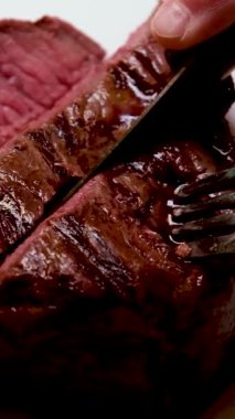 Bifteği ikiye böldüm. Tahta bir kesme tahtasının üzerinde bıçakla. Yakın çekim, orta kıvrımlı. Yüksek kalite 4k görüntü