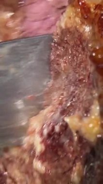 bbq, kebap büyük bir parça sulu eti büyük bir bıçakla kesti. Küçük demir spatula yağıyla tabaktan çıkarıyorlar. Kan akıyor.