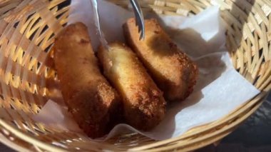 Özel cımbız kullanan genç bir kız, pencerenin yanındaki hamurda kızarmış muz yer. Saçı düzeltir. Etraftaki her şeyi inceler.