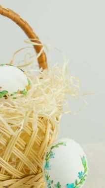 Easter holiday decorative handmade eggs in wicker basket on white table white background embroidery ribbons on eggs ornament blue green yellow color postcard gift congratulations invitation
