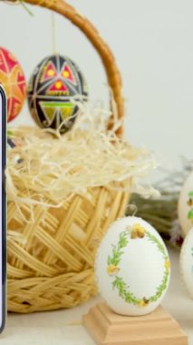 Paskalya kompozisyonu telefon ile beyaz krom anahtar ekranlı yumurta sepeti ve lavanta rengi yumurta boyalı lavanta çiçekleri tahta bardak altlıkları beyaz arka planda Paskalya tatili