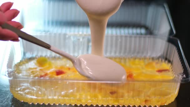 自宅でベリーでゼリーケーキを調理すると ブレンダーで美味しいデザートビートの層が注がれます プラスチック容器のおいしいデザートでテーブルスプーンで滑らかにブルーベリーゼリームースを注ぐ — ストック動画