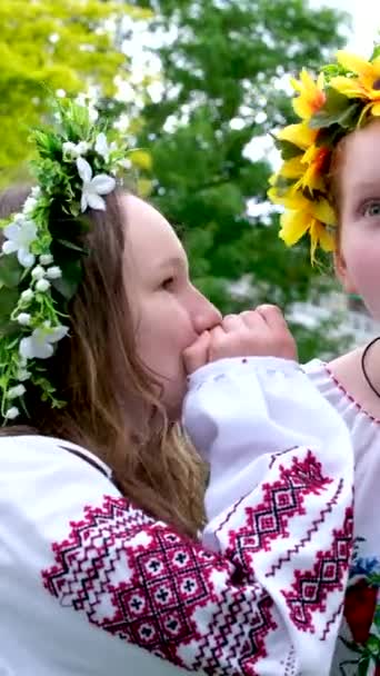 美丽的年轻女子编织着花环 在公园里聊天 在花园里绣着民族乌克兰语衬衫 环绕着向日葵花和森林的白花 — 图库视频影像