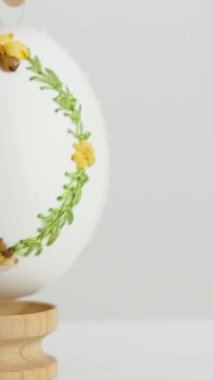 close-up of an embroidered egg on the eggshell of goose eggs female hand slowly puts it on a wooden stand on white background krashenka drawings ornaments scenery easter celebration