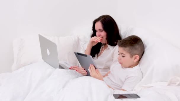 담요를 엄마와 아들은 온라인으로 네트워크를 즐기는 아이의 부드러운 침대에 있습니다 — 비디오