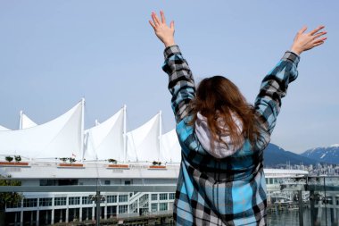 Neşeli bir genç kız güzel bir elbiseyle Kanada City Vancouver yolcu gemisinin arka planında duruyor. Elini kaldırdı. Kanada 'nın başkenti Vancouver' a seyahat acentesinin reklamını yapabilirsiniz.
