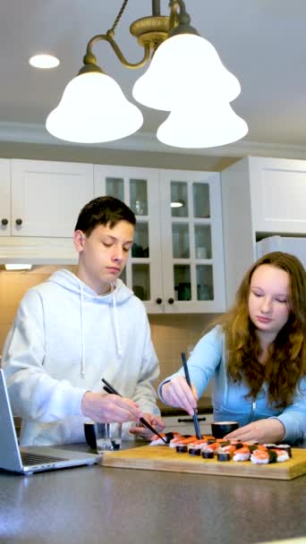 ティーンエイジャー男の子と女の子食べる寿司で自宅でキッチンで映画を見ますラップトップの花ブドウ美しい環境リンゴ美しいですホワイトルーム最初の日付通信会議の友人 — ストック動画