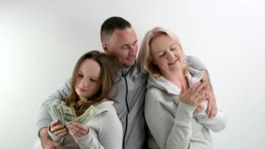 Mutlu zengin aile para sayar. Kızın dolarları var. Annenin de Euro 'su var. Ailenin babası beyaz arka planda her iki taraftaki kadınlara sarılıyor. Bir tomar para, bir fırsat.