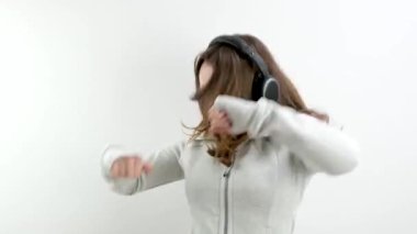 Hızlı ve kızgın moda dansçısı genç kız kollarını sallayarak beyaz bir arka planda kulaklıkla güçlü bir şekilde şarkı söylüyor öfke ifadeleri ergenlik çağındaki moda havalılığının dışavurumları. öfke