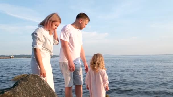 快乐的家庭在海滨庆祝小女孩的生日妈妈带着一个盒子和一个蛋糕女孩打开礼物爸爸 妈妈哥哥和姐姐在海滨 在一个阳光灿烂的日子 — 图库视频影像