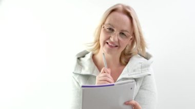 Gözlüklü Avrupalı bir kadın kağıt kağıtlara kalem ısırıyor. Hikaye yazarı dergisi tasarımı ile meditasyon yapıyor. Stüdyoda beyaz arka planda sarı saçlar düşünüyor. kitabın yazarı