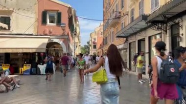 Korfu adasındaki dar sokaklar boyunca uzanan sarı binalar mıknatısların etrafında dolanıyor. Satış hayatı turistik bir şehirde, gökyüzünde yüksek binalarda, Yunanistan 09.09.2023