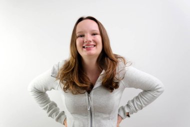 Beyaz duvarın arkasında beyaz, çekici bir kız omuzlarını kaldırırken pastel gömlek giyiyor. Yüksek kalite 4k görüntü