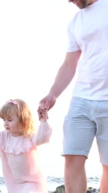 Neşeli baba küçük kızıyla yürüyor. Üç yaşında bir kız etrafına bakıyor. Parmağını kumsalda gezdiriyor. Kardeşlerin bacakları görünür bir aile sevgisi.