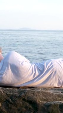 Genç bir çocuk kumsalda yatıyor. Büyük Taş Sahili 'nde güneşli okyanus istirahatı, dinlenme rüyaları. Başının altına spor ayakkabı şortu koy. ve gençlik tişörtleri.