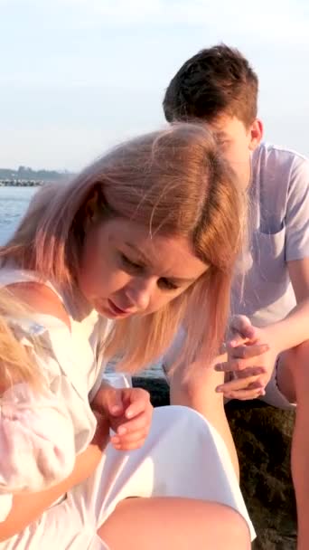 快乐的家庭在海滨庆祝小女孩的生日妈妈带着一个盒子和一个蛋糕女孩打开礼物爸爸 妈妈哥哥和姐姐在海滨 在一个阳光灿烂的日子 — 图库视频影像