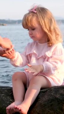 Pembe elbiseli, güzel bir kızın yanında küçük şirin bir kız. Pasta yiyor ve annesi peçeteyle ellerini siliyor. Küçük bir çocuk.