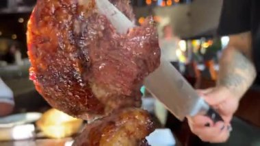 Et lokantası kesilmiş ızgara et büyük bir parça ile restoranın arka planında masanın üzerinde büyük bir bıçak tanınmayan insanlar görünüyor Kafe bira et dana eti sulu oturuyor. orta pişmiş