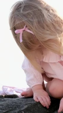 Küçük kız elleriyle dünyayı keşfediyor. Taştaki böceklerin yaşayan canlılarını arıyor. Sahilde oturuyor. Pembe kurdeleli çocuk, yetişkin gözetiminde olmadan yalnız bırakılır.
