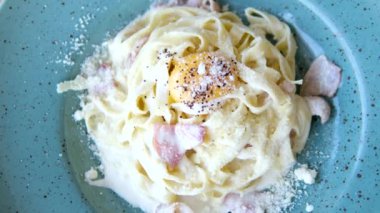 Makarnayı bir tabaktan carbonara sosuyla alan çatala yakın çekim. Çatallı sıcak spagetti. İtalyan mutfağı ve ev yemeği konsepti. Yüksek kalite 4k görüntü